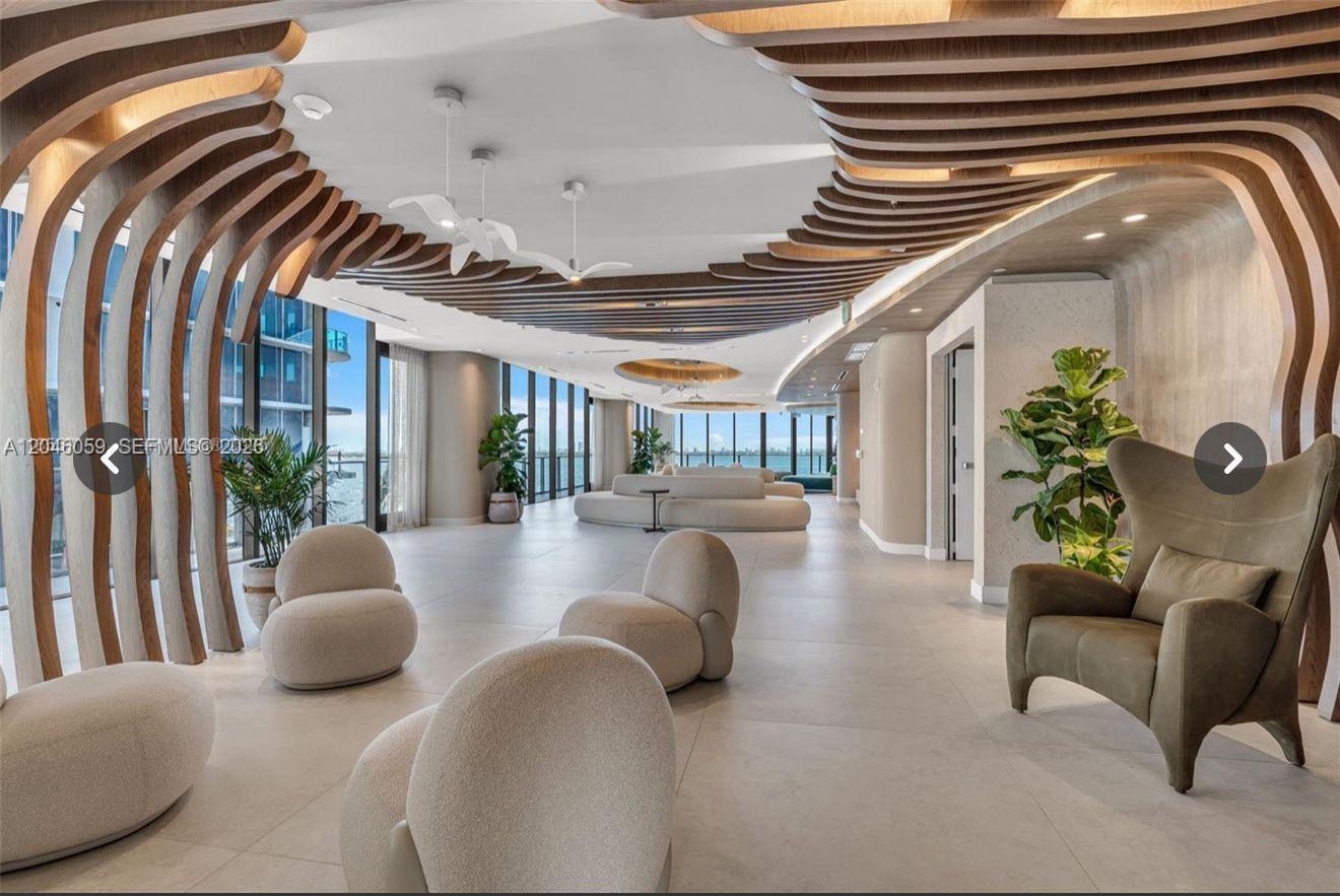 A modern lounge area features curved wooden ceiling slats, neutral furniture, and floor-to-ceiling windows — 725 NE 24 St # 401, Miami FL 33137, MIAMI, FL