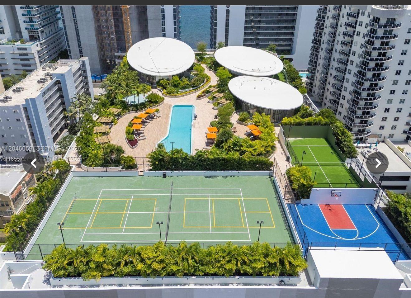 An aerial view of a rooftop amenity deck featuring a pool, tennis court, and basketball court — 725 NE 24 St # 401, Miami FL 33137, MIAMI, FL