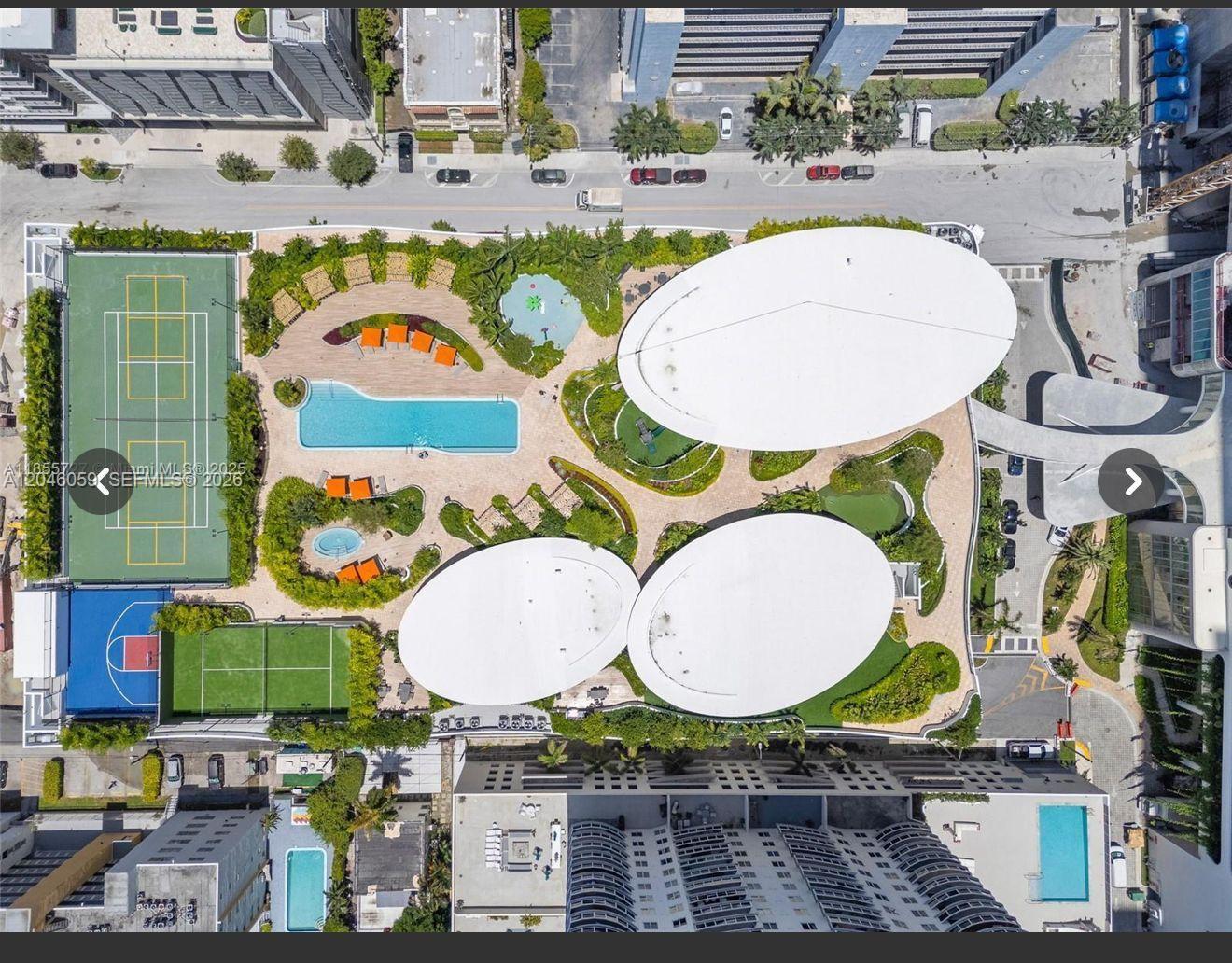 Aerial view of a residential building rooftop featuring a tennis court, pool, and white structures — 725 NE 24 St # 401, Miami FL 33137, MIAMI, FL