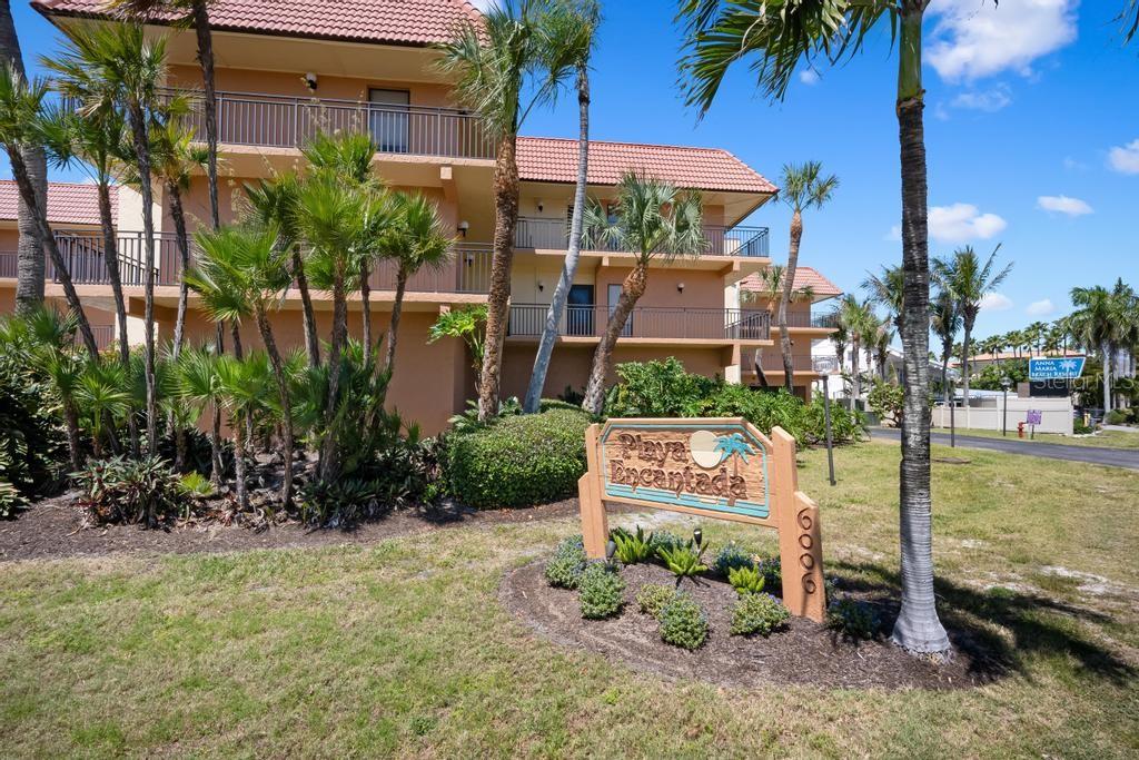 A three-story tan apartment building with balconies stands behind a Playa Encantada sign — 6005 GULF DRIVE UNIT 219, HOLMES BEACH, FL