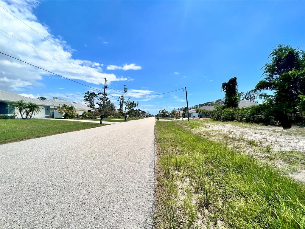 A paved residential street stretches into the distance between houses and an undeveloped grassy lot — 228 FAIRWAY ROAD, ROTONDA WEST, FL