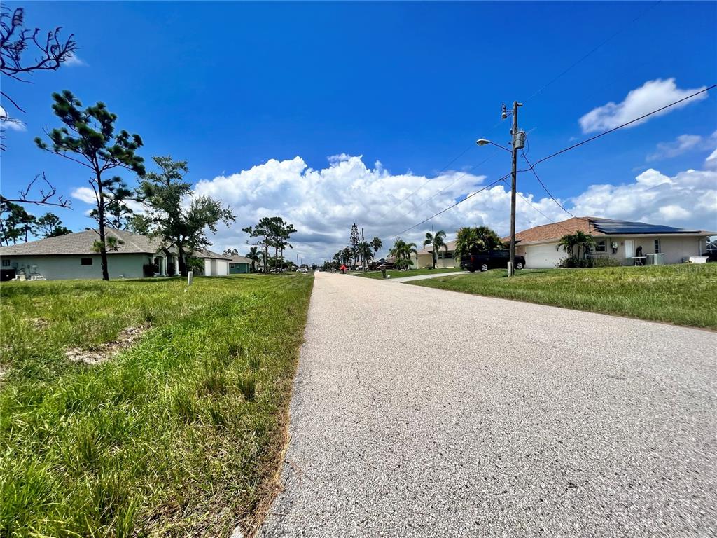 A paved residential street stretches between grassy lots and single-story houses under a blue sky — 228 FAIRWAY ROAD, ROTONDA WEST, FL
