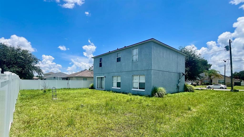 The exterior of a two-story stucco house with a grassy backyard and white fence — 703 ROBIN COURT, KISSIMMEE, FL