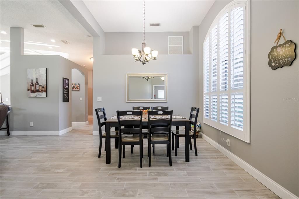 A dining room features a dark wood table and chairs, a chandelier, and plantation shutters — 1001 ENGLISH BLUFFS COURT, BRANDON, FL