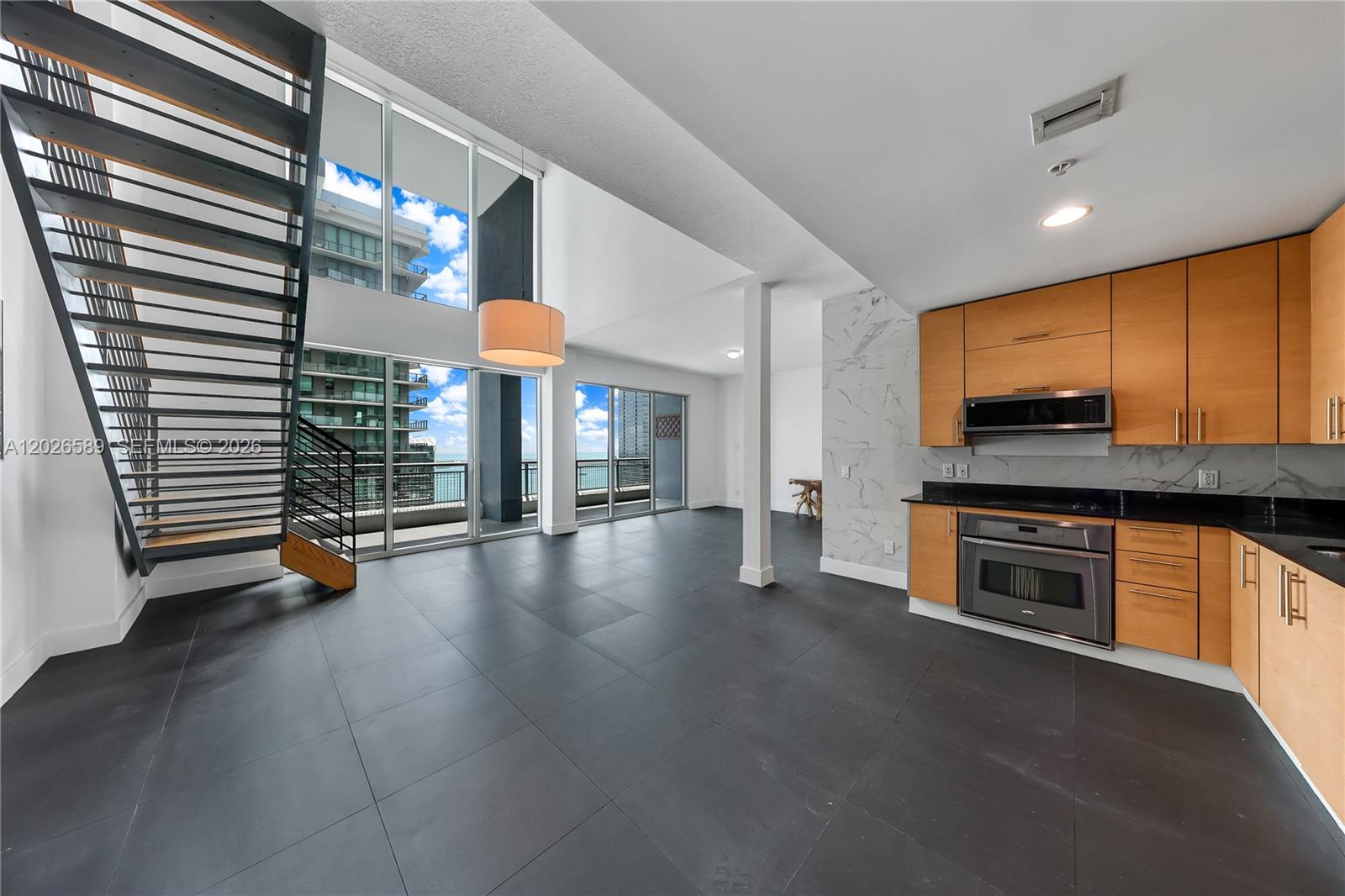 A modern kitchen and living area feature dark tile floors, light wood cabinets, and a staircase — 60 SW 13th St # 4404, Miami FL 33130, MIAMI, FL