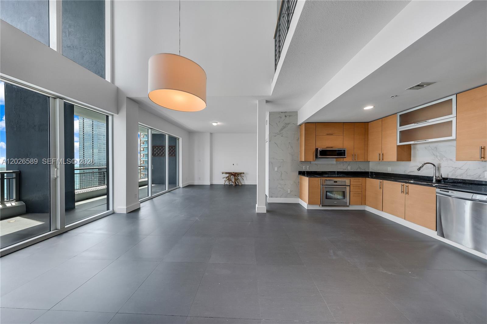 A modern kitchen with light wood cabinets and dark countertops opens to a spacious living area — 60 SW 13th St # 4404, Miami FL 33130, MIAMI, FL