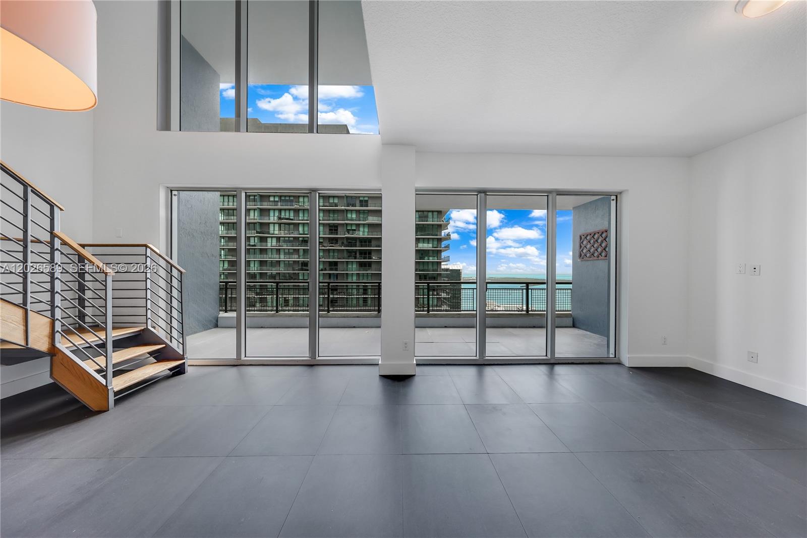 A modern living room features dark tile floors, a floating staircase, and floor-to-ceiling balcony windows — 60 SW 13th St # 4404, Miami FL 33130, MIAMI, FL