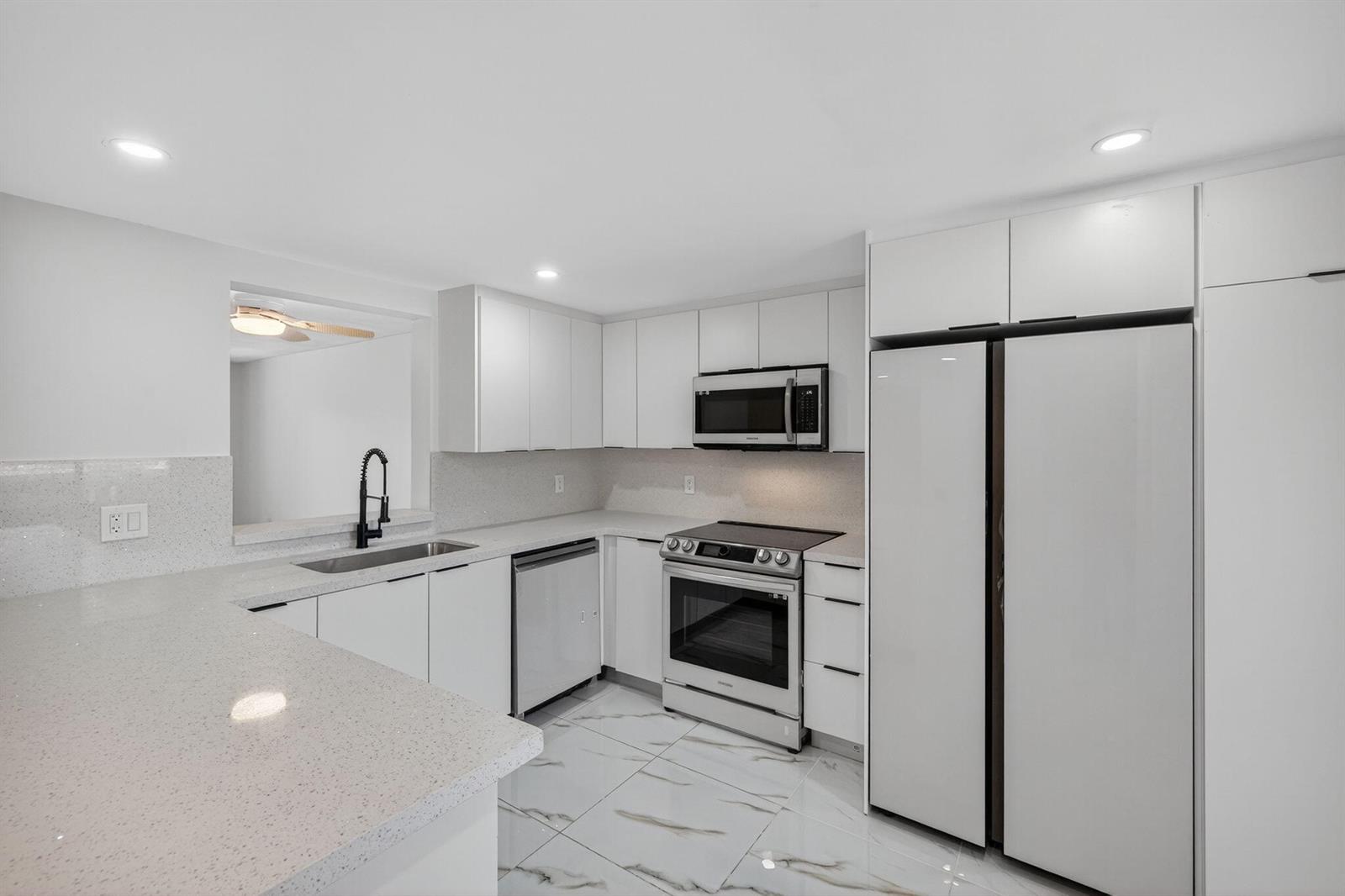 A modern white kitchen features stainless steel appliances, quartz countertops, and marble-patterned tile flooring — 14375 Strathmore Lane # 303, Delray Beach FL 33446, DELRAY BEACH, FL