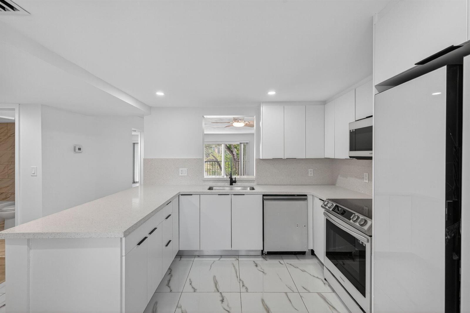 A modern white kitchen features quartz countertops, stainless steel appliances, and marble-patterned tile flooring — 14375 Strathmore Lane # 303, Delray Beach FL 33446, DELRAY BEACH, FL