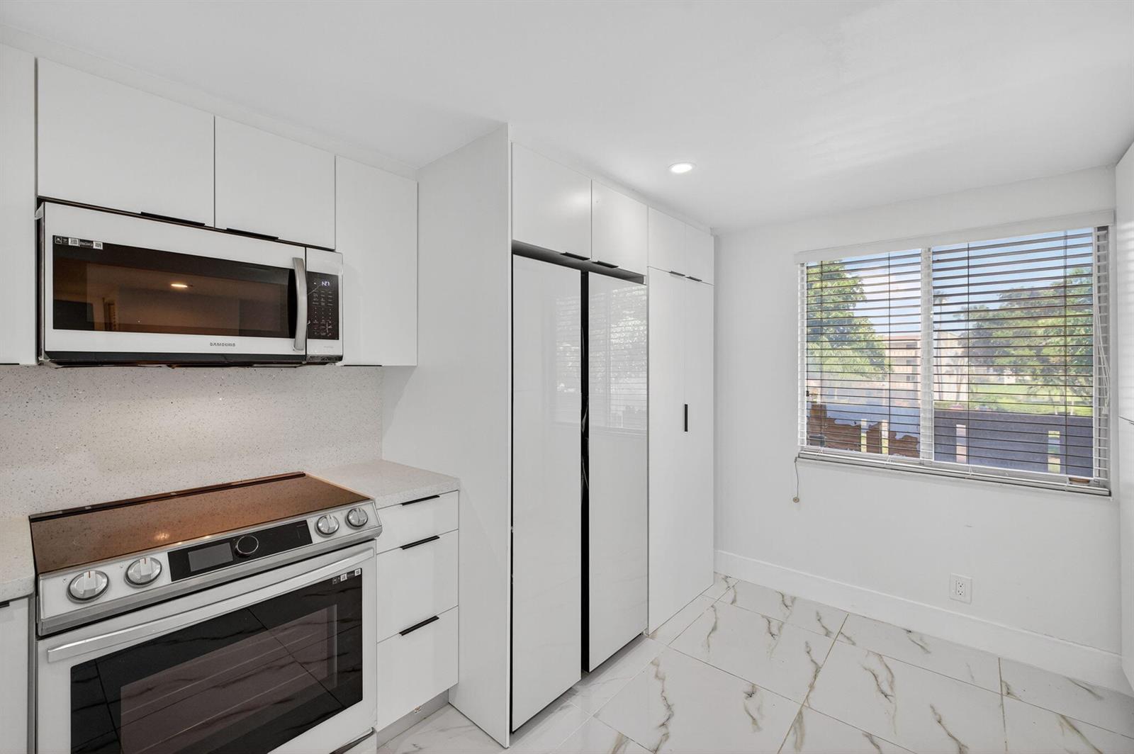A modern kitchen features white cabinetry, stainless steel appliances, and white marble-patterned tile flooring — 14375 Strathmore Lane # 303, Delray Beach FL 33446, DELRAY BEACH, FL