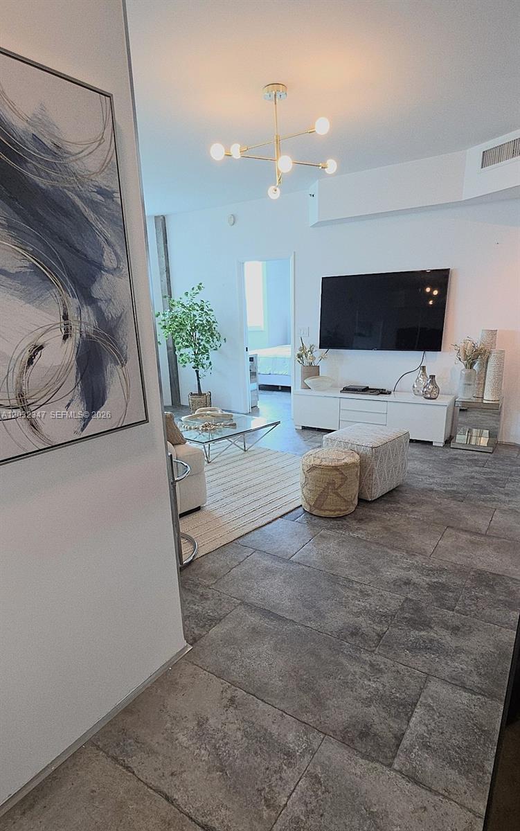 A living room features a wall-mounted television, a modern chandelier, and large gray floor tiles — 300 S Pointe Dr # 908, Miami Beach FL 33139, MIAMI BEACH, FL