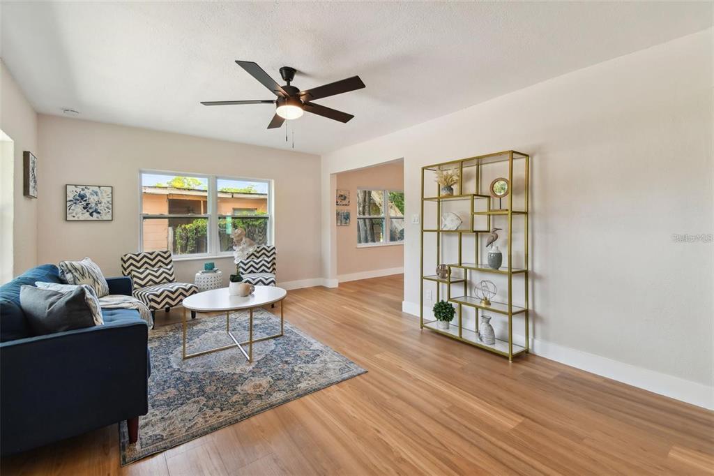 A living room features wood-look flooring, a blue sofa, patterned chairs, and a gold bookshelf — 1826 30TH STREET S, ST PETERSBURG, FL