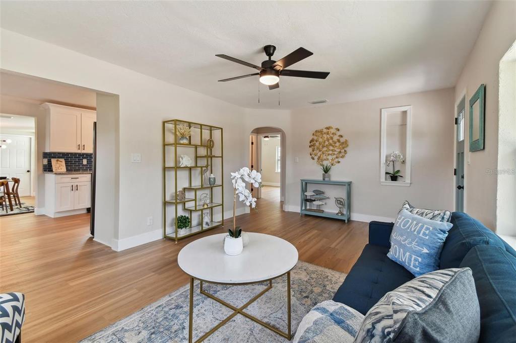 A living room features light wood floors, a blue sofa, and a gold metal shelving unit — 1826 30TH STREET S, ST PETERSBURG, FL