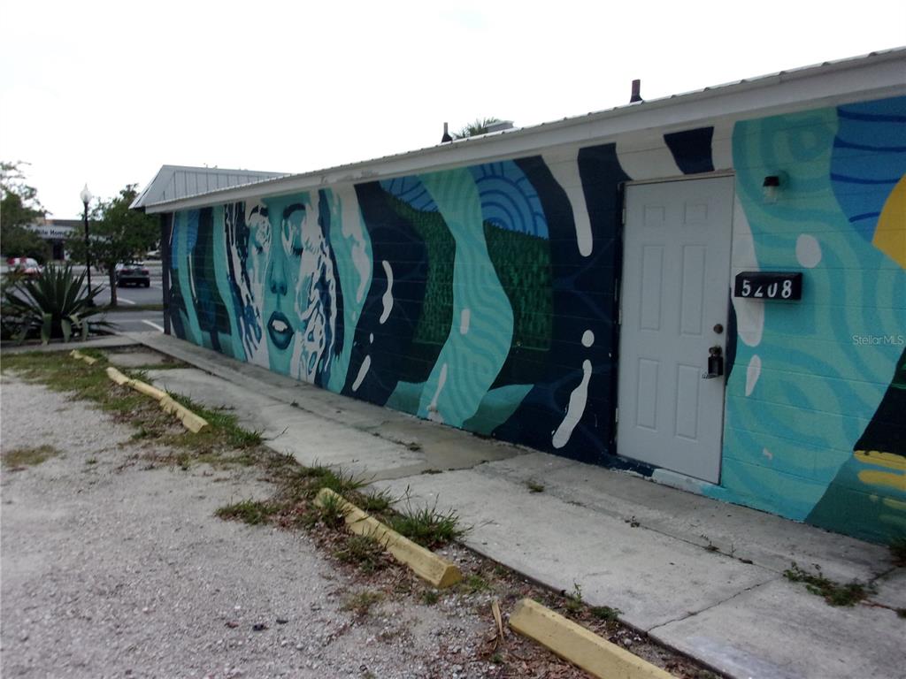 A white building exterior features a large blue mural of a face next to a door — 5206 7TH STREET, ZEPHYRHILLS, FL