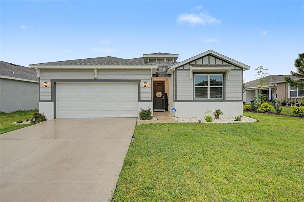 A single-story house with a two-car garage, gray siding, and a stone-accented entryway — 7815 WHEAT STONE DRIVE, ZEPHYRHILLS, FL