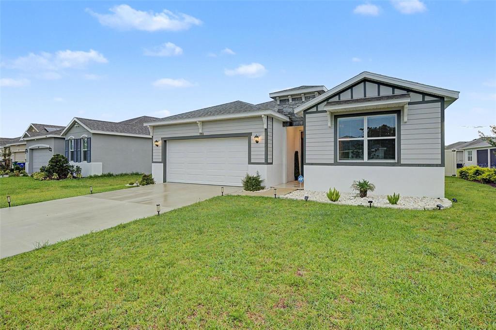 A single-story suburban house with a gray exterior, two-car garage, and a manicured front lawn — 7815 WHEAT STONE DRIVE, ZEPHYRHILLS, FL