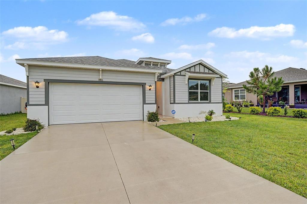 A single-story house with light gray siding, a white garage door, and a concrete driveway — 7815 WHEAT STONE DRIVE, ZEPHYRHILLS, FL