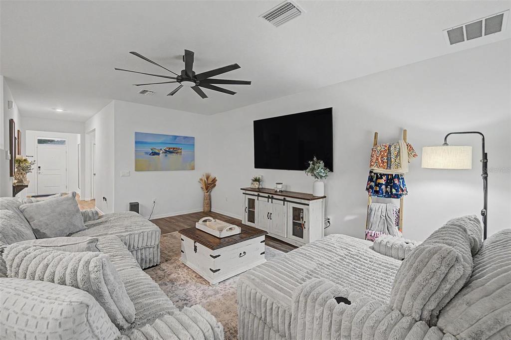 A living room features grey textured sofas, a white media console, and a ceiling fan — 7815 WHEAT STONE DRIVE, ZEPHYRHILLS, FL