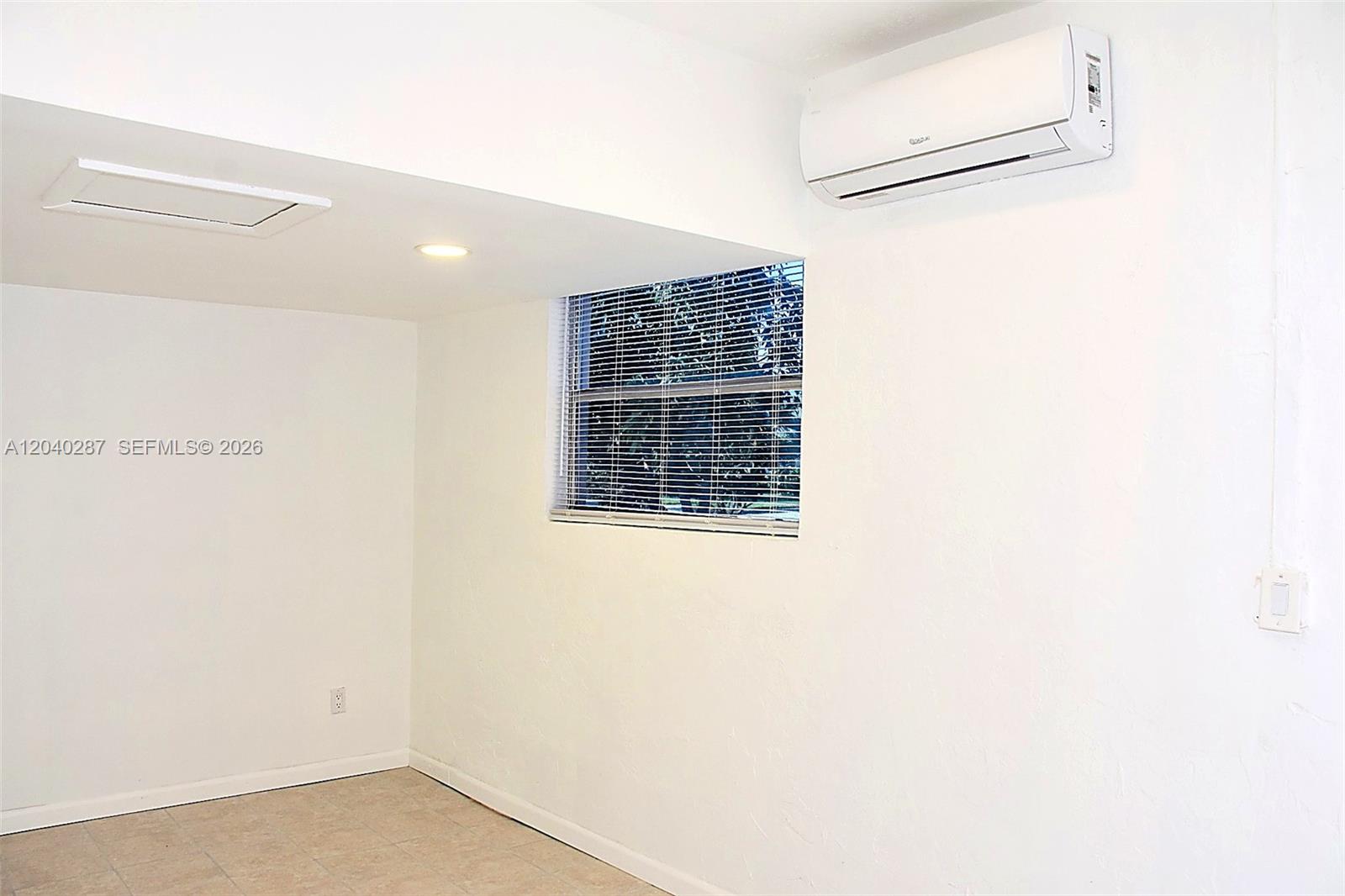A room with white walls, tiled flooring, a window with blinds, and a wall-mounted air conditioner — MARGATE, FL