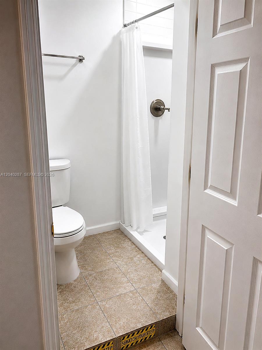 A small bathroom features a toilet, a shower stall with a curtain, and tiled flooring — MARGATE, FL