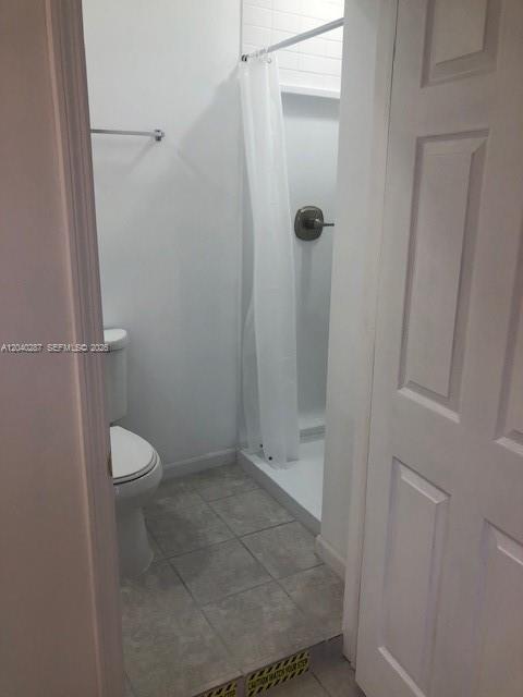 A small bathroom features a white toilet, a tiled floor, and a shower stall — MARGATE, FL