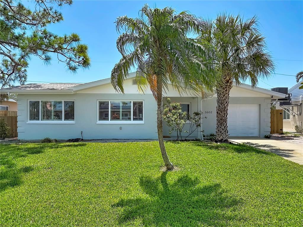 A single-story house with a light blue exterior, a palm tree, and a front lawn — 3602 CASABLANCA AVENUE, ST PETE BEACH, FL