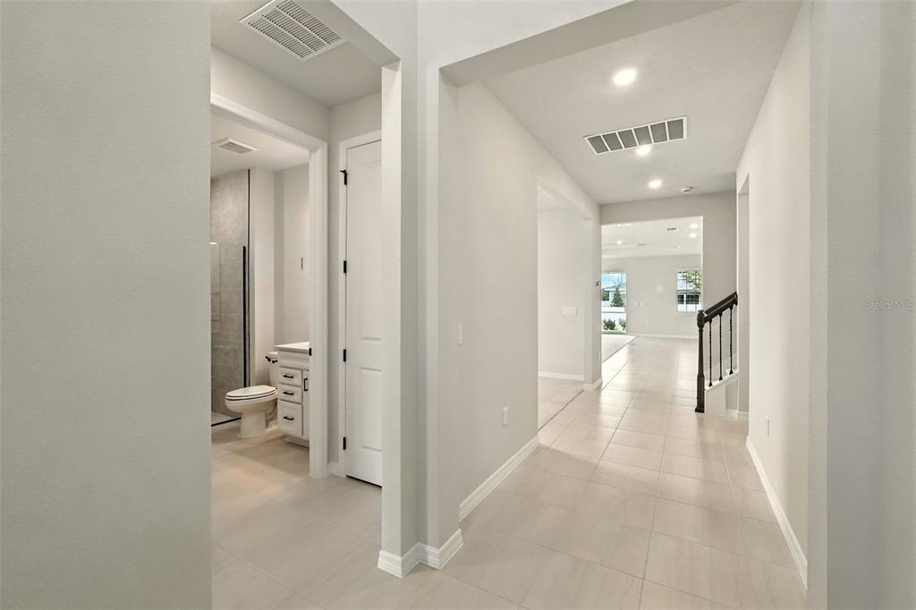 A hallway with light tile flooring leads toward a bathroom and a staircase — 276 SUMMER PINE STREET, WINTER GARDEN, FL