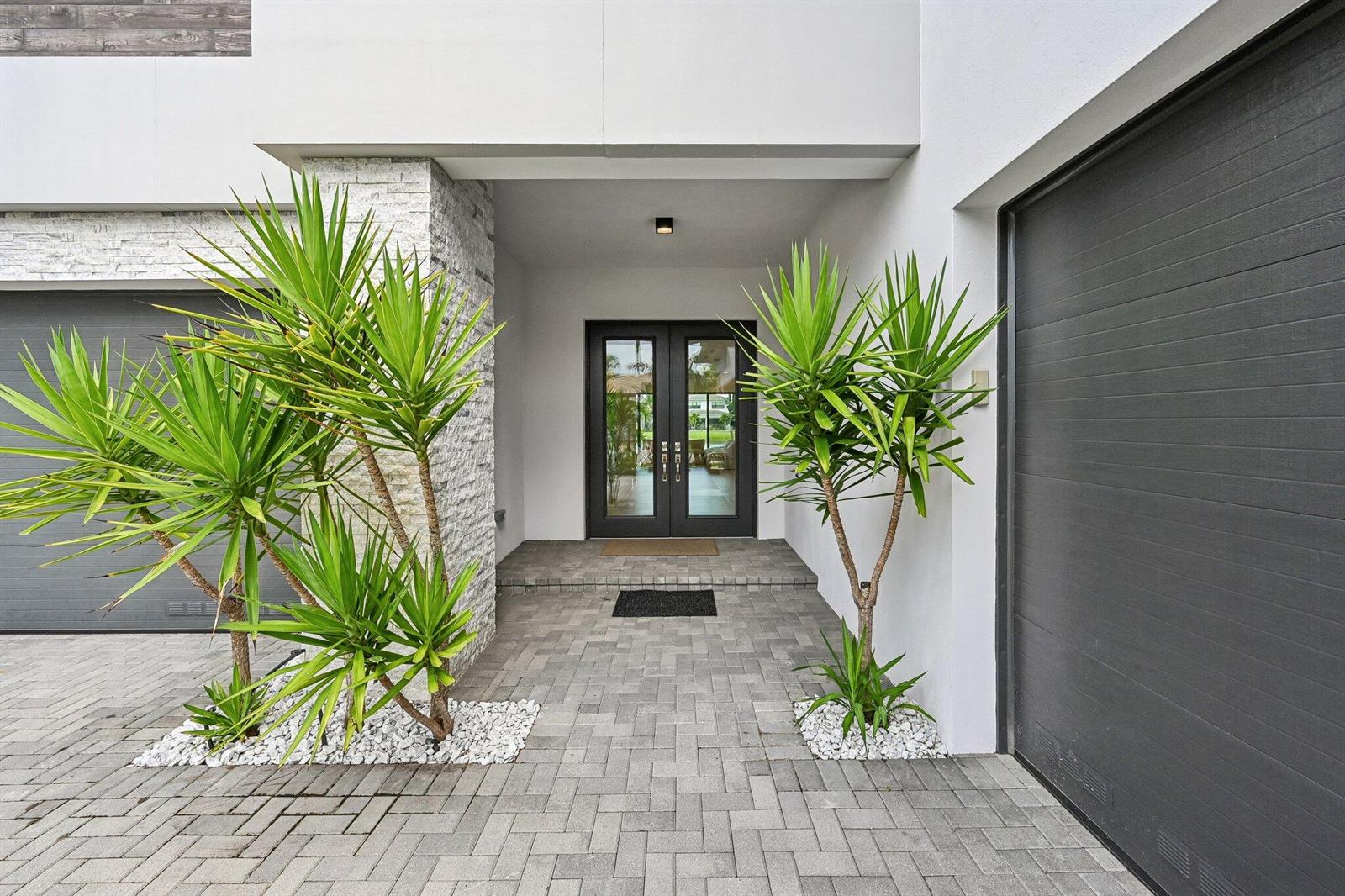 A modern home entrance features a paved walkway, double glass doors, and two yucca plants — 17070 Rainbow Falls Trail, Boca Raton FL 33496, BOCA RATON, FL