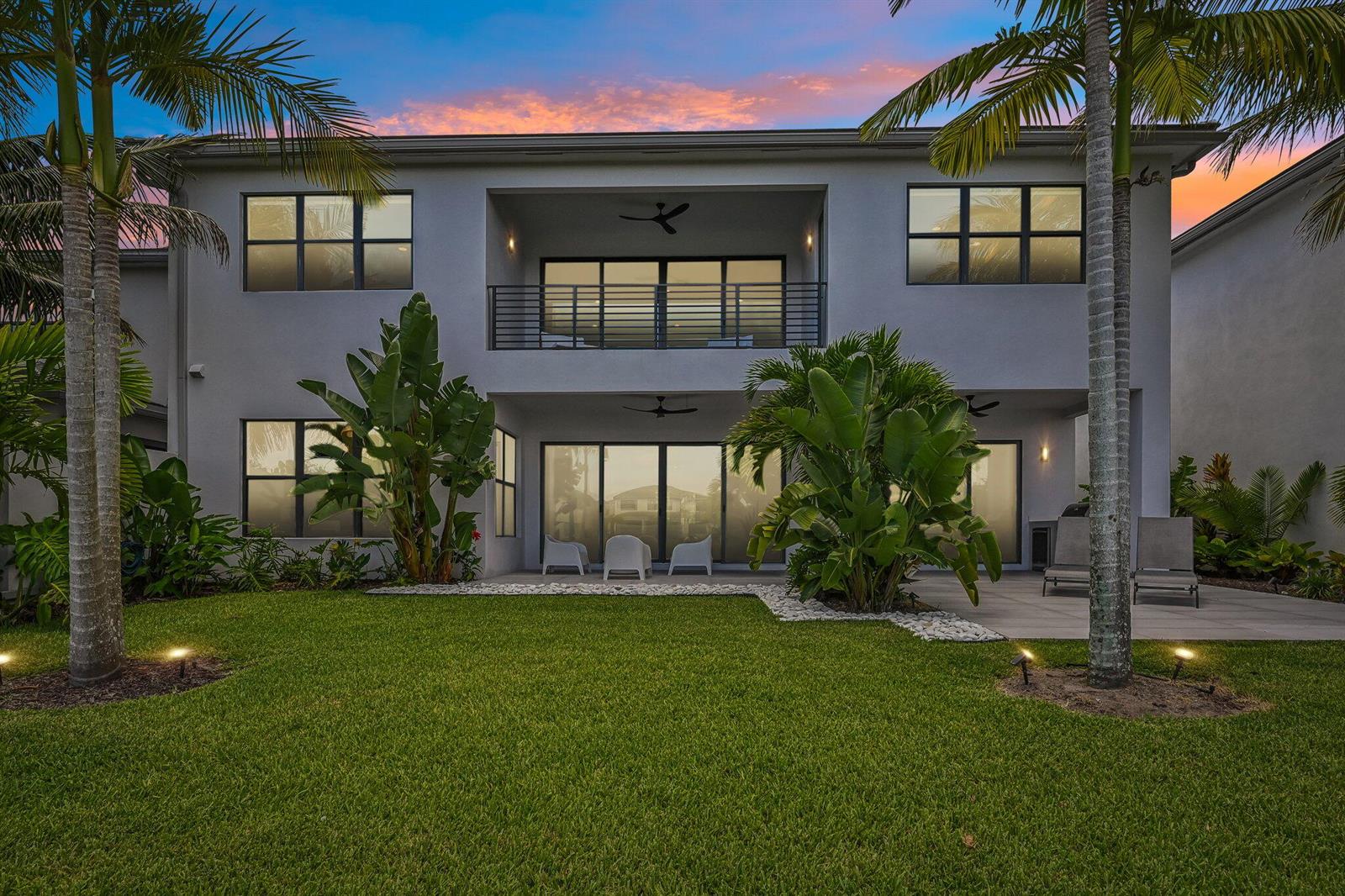 A two-story house exterior features a balcony, large windows, and a landscaped backyard at sunset — 17070 Rainbow Falls Trail, Boca Raton FL 33496, BOCA RATON, FL