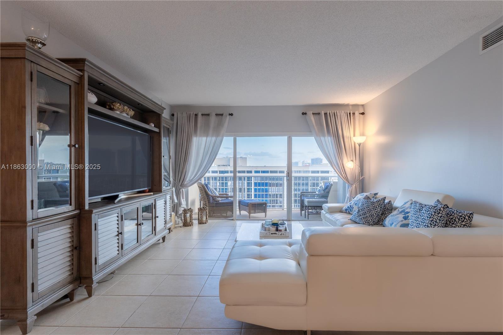 A living room features a large entertainment center, white sectional sofa, and a balcony view — 1985 S Ocean Dr # 15G, Hallandale Beach FL 33009, HALLANDALE BEACH, FL