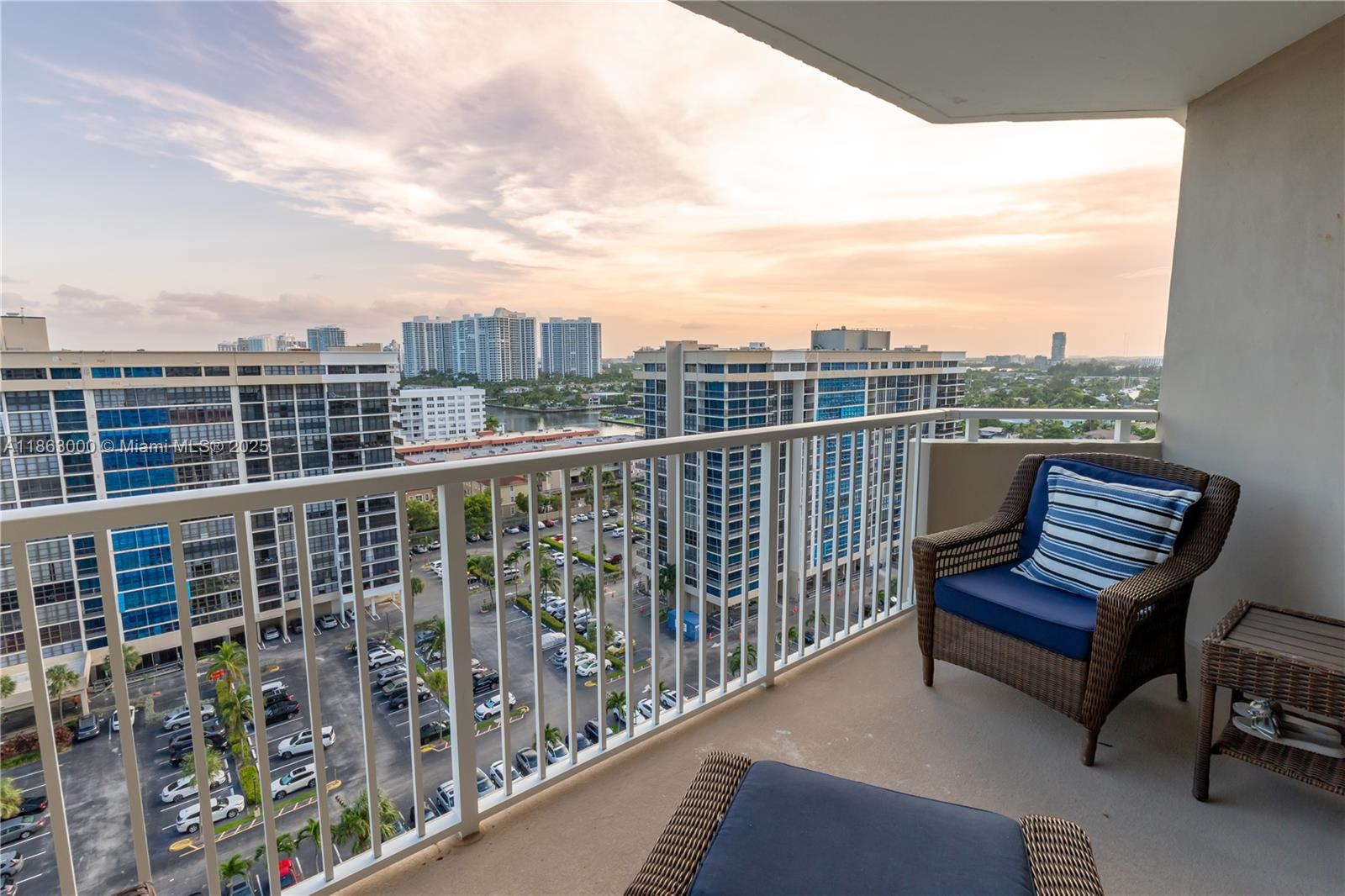 A balcony with wicker furniture overlooks a parking lot and surrounding high-rise buildings — 1985 S Ocean Dr # 15G, Hallandale Beach FL 33009, HALLANDALE BEACH, FL