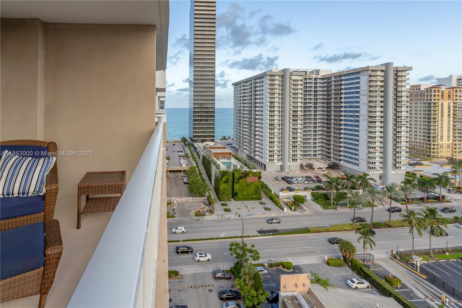 A balcony with wicker furniture overlooks a street, parking lots, and high-rise buildings near the ocean — 1985 S Ocean Dr # 15G, Hallandale Beach FL 33009, HALLANDALE BEACH, FL