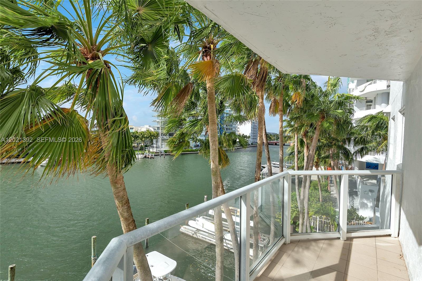 A balcony with a glass railing overlooks a canal lined with palm trees and boats — 5900 Collins Ave # 408, Miami Beach FL 33140, MIAMI BEACH, FL