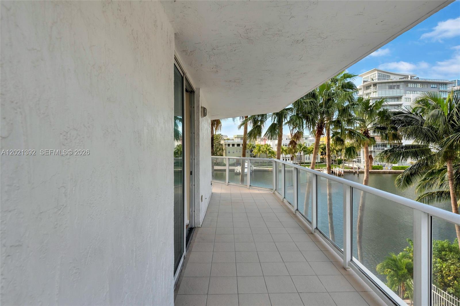 A tiled balcony with a glass railing overlooks a canal and palm trees — 5900 Collins Ave # 408, Miami Beach FL 33140, MIAMI BEACH, FL