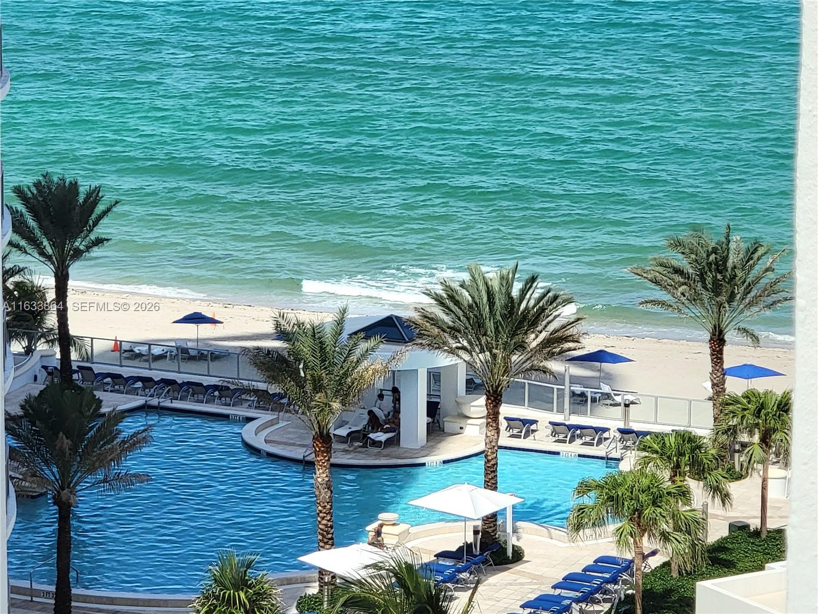 An elevated view of a swimming pool area with palm trees and a sandy beach — 3505 S Ocean Dr # 1105, Hollywood FL 33019, HOLLYWOOD, FL