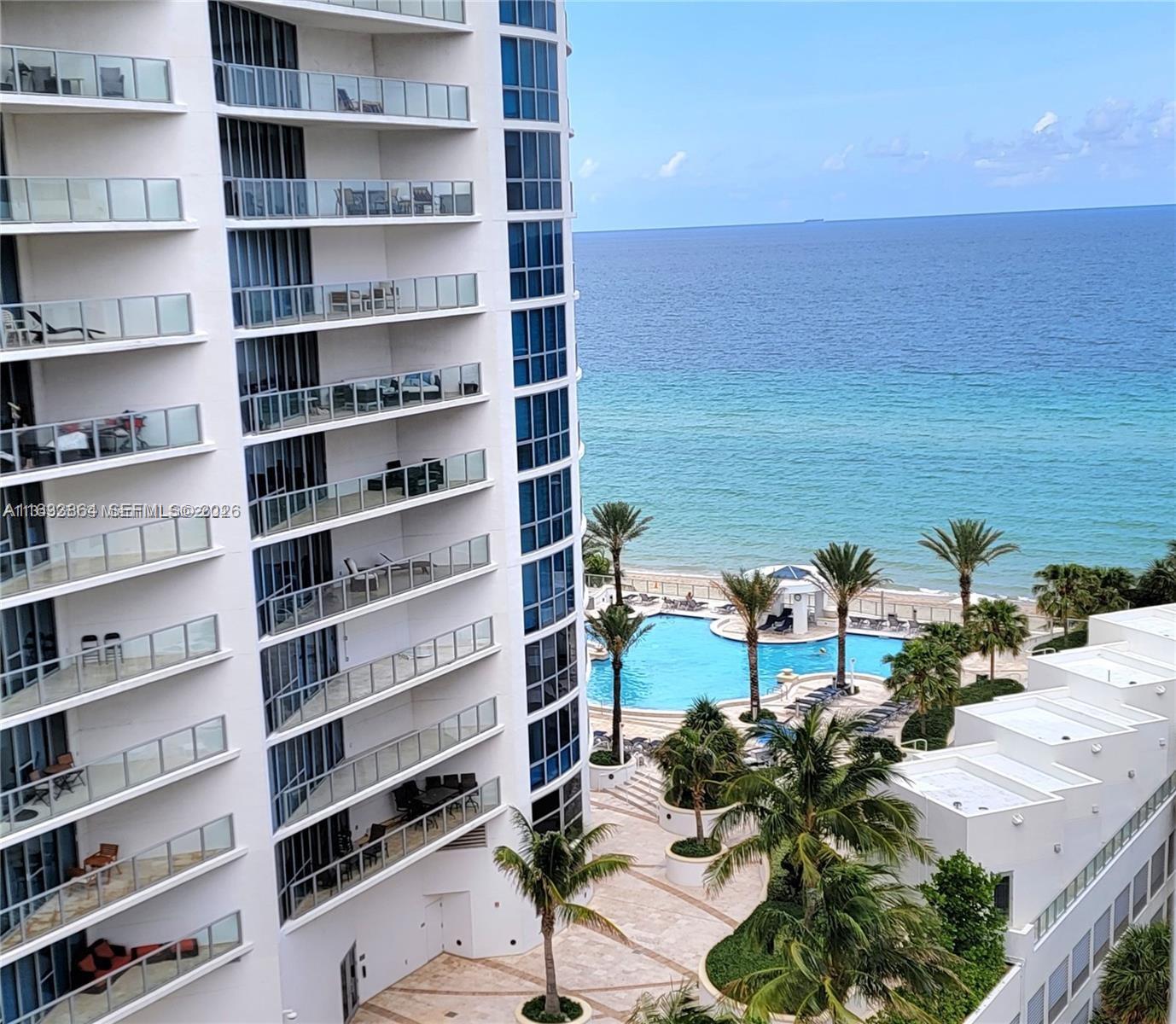 A high-rise building overlooks a swimming pool, palm trees, and the ocean — 3505 S Ocean Dr # 1105, Hollywood FL 33019, HOLLYWOOD, FL