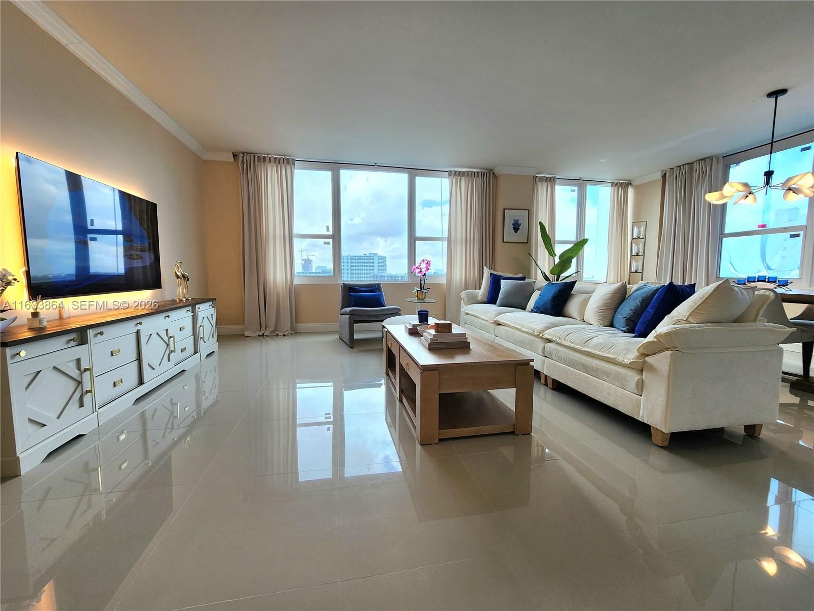 A bright living room features a large white sofa, wooden coffee table, and television console — 3505 S Ocean Dr # 1105, Hollywood FL 33019, HOLLYWOOD, FL