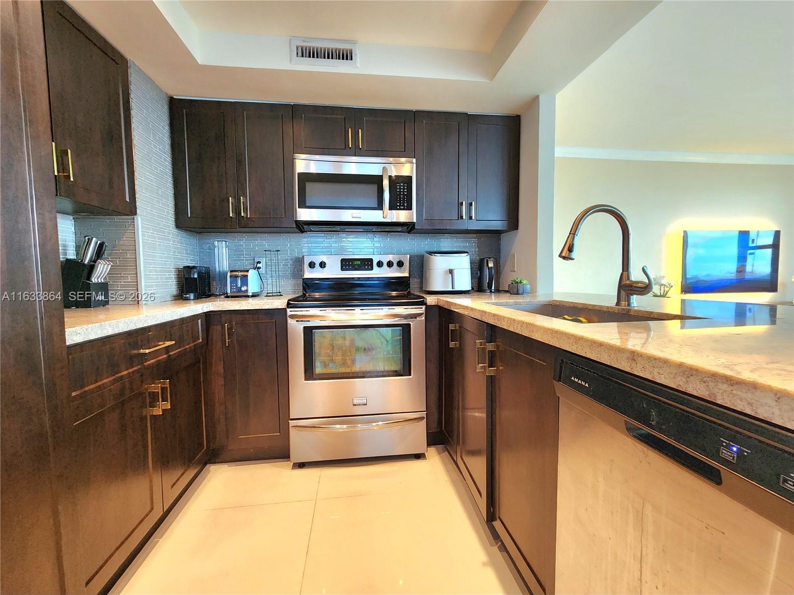 A kitchen features dark wood cabinets, stainless steel appliances, and light-colored granite countertops — 3505 S Ocean Dr # 1105, Hollywood FL 33019, HOLLYWOOD, FL
