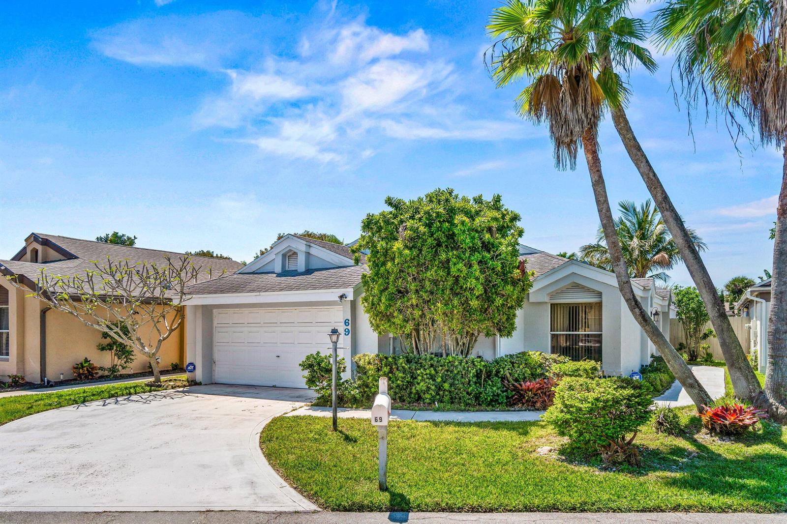 A single-story house with a white garage, a large green bush, and palm trees — 69 King Fisher Way, Boynton Beach FL 33436, BOYNTON BEACH, FL