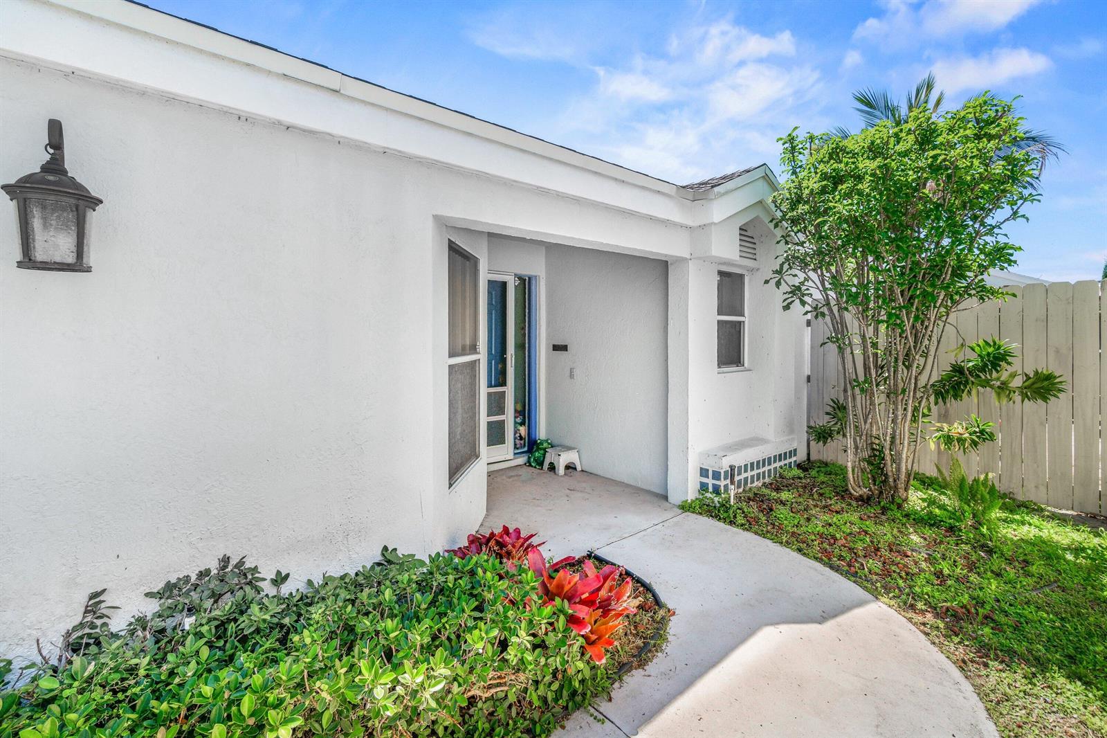 A white stucco house exterior features a covered entryway, a small garden, and a fence — 69 King Fisher Way, Boynton Beach FL 33436, BOYNTON BEACH, FL