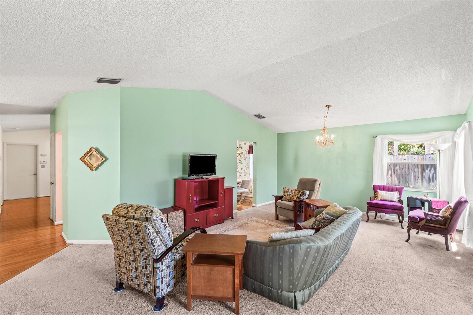 A living room with mint green walls, carpeted flooring, and a vaulted ceiling — 69 King Fisher Way, Boynton Beach FL 33436, BOYNTON BEACH, FL