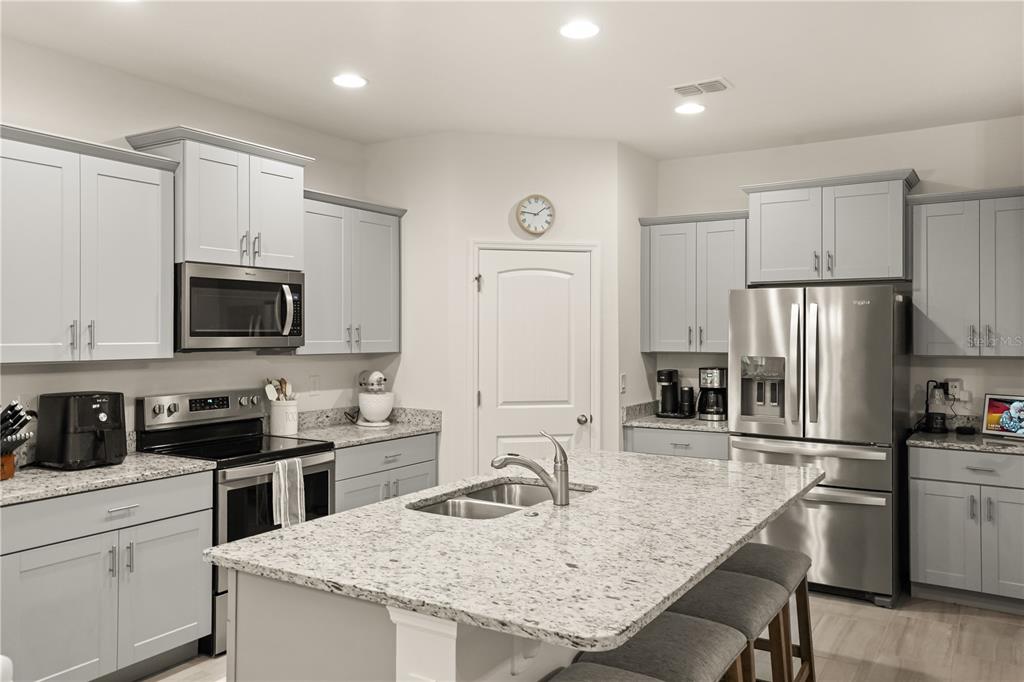 A modern kitchen features light gray cabinets, granite countertops, a center island, and stainless appliances — 16161 MANGROVE ROAD, WINTER GARDEN, FL
