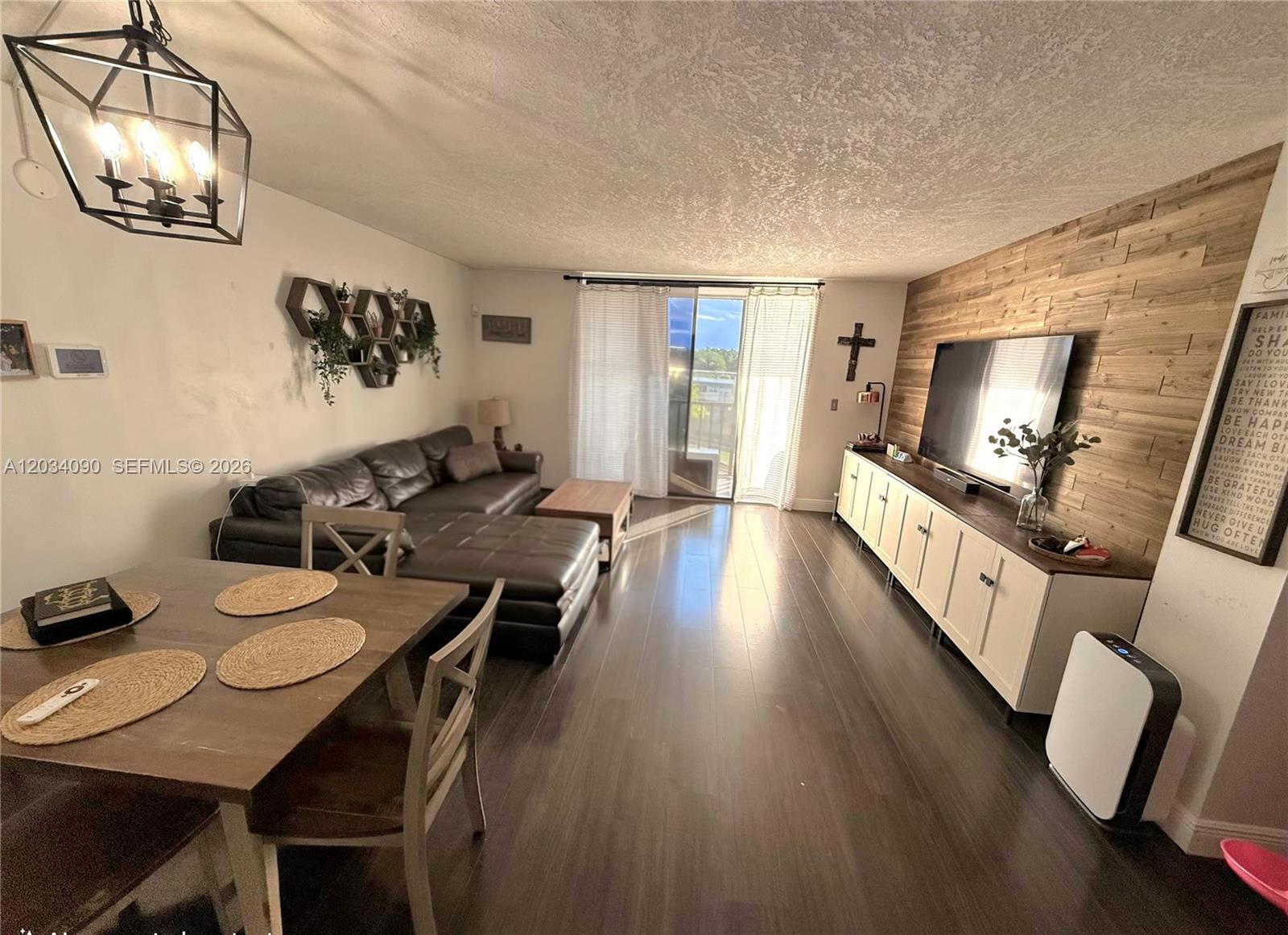 A living and dining area features dark wood flooring, a wood-paneled accent wall, and a sectional — 8520 SW 133rd Ave Rd # 424, Miami FL 33183, MIAMI, FL