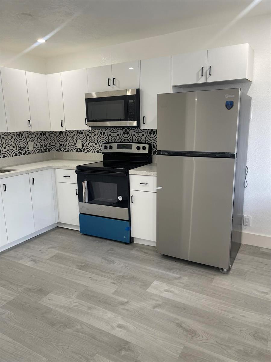 A kitchen features white cabinets, stainless steel appliances, and a patterned black and white backsplash — 880 NW 8th Avenue, Pompano Beach FL 33060, POMPANO BEACH, FL