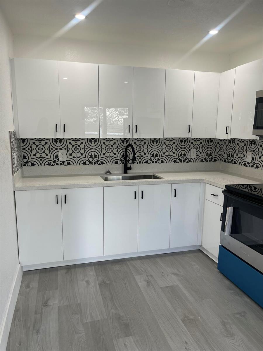 A kitchen with white high-gloss cabinets, a patterned backsplash, and light gray wood-look flooring — 880 NW 8th Avenue, Pompano Beach FL 33060, POMPANO BEACH, FL