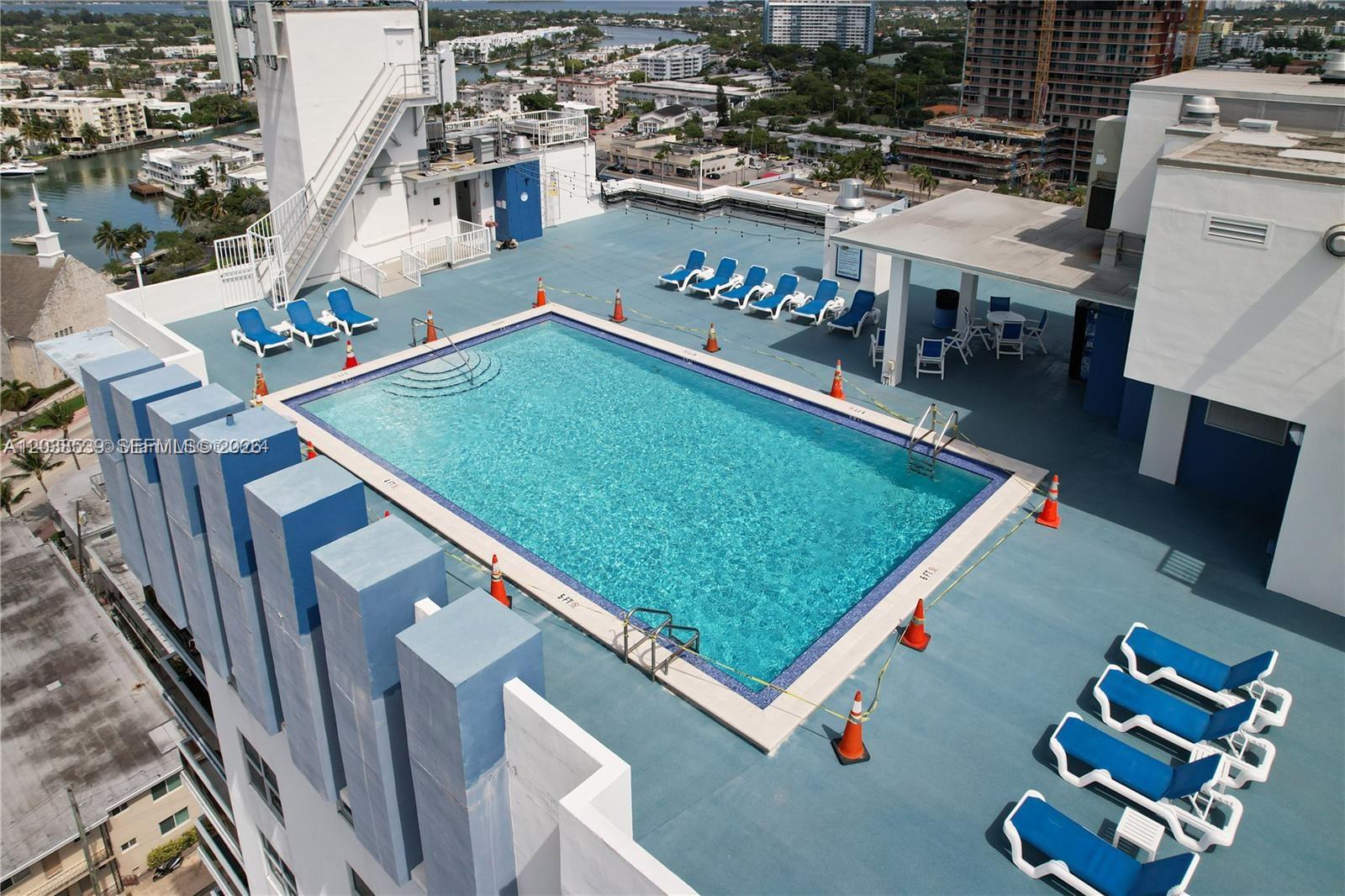 An aerial view shows a tall apartment building with a rooftop pool and parking lot — 401 69th St, Miami Beach FL 33141, MIAMI BEACH, FL