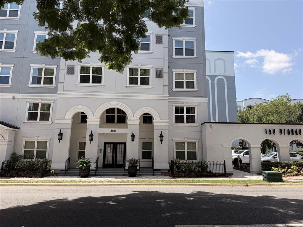 The exterior of a multi-story apartment building features arched entryways and a paved street — 304 E SOUTH STREET UNIT 6028, ORLANDO, FL