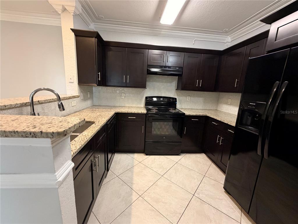 A kitchen features dark wood cabinets, granite countertops, black appliances, and light-colored tile flooring — 304 E SOUTH STREET UNIT 6028, ORLANDO, FL