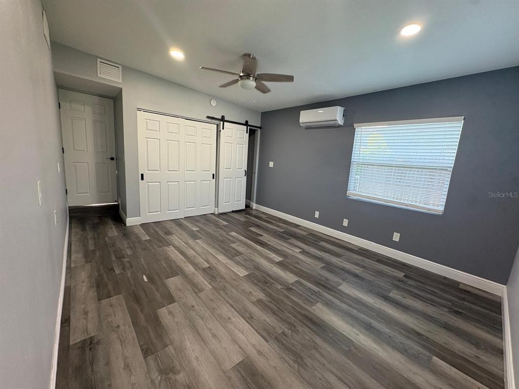 A bedroom features gray walls, wood-look flooring, a ceiling fan, and a sliding barn door — 14347 DELMAR STREET, DADE CITY, FL