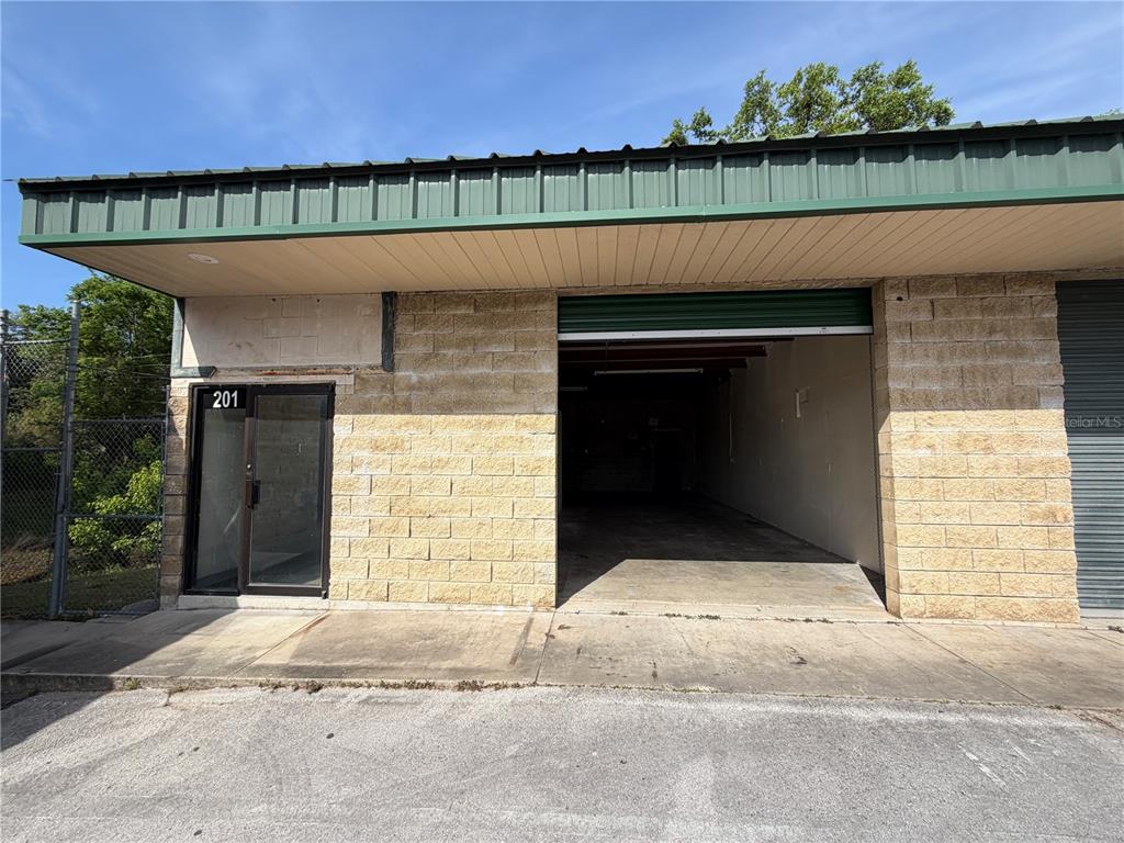 An exterior view of a commercial building with a glass door and an open bay — 1706 N MAGNOLIA AVENUE UNIT 201, OCALA, FL